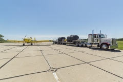 Trailer hauled by semi-truck near an airplane on a runway