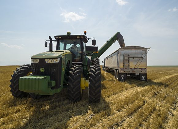 a large green tractor dumping grain into a trailer and other Used Trailers, Grain Trailer Sales, and Hopper Trailers for Sale in Grand Forks, ND